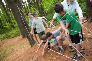 A group of children working through a rope obstacle at a summer camp for neurodivergent children.  