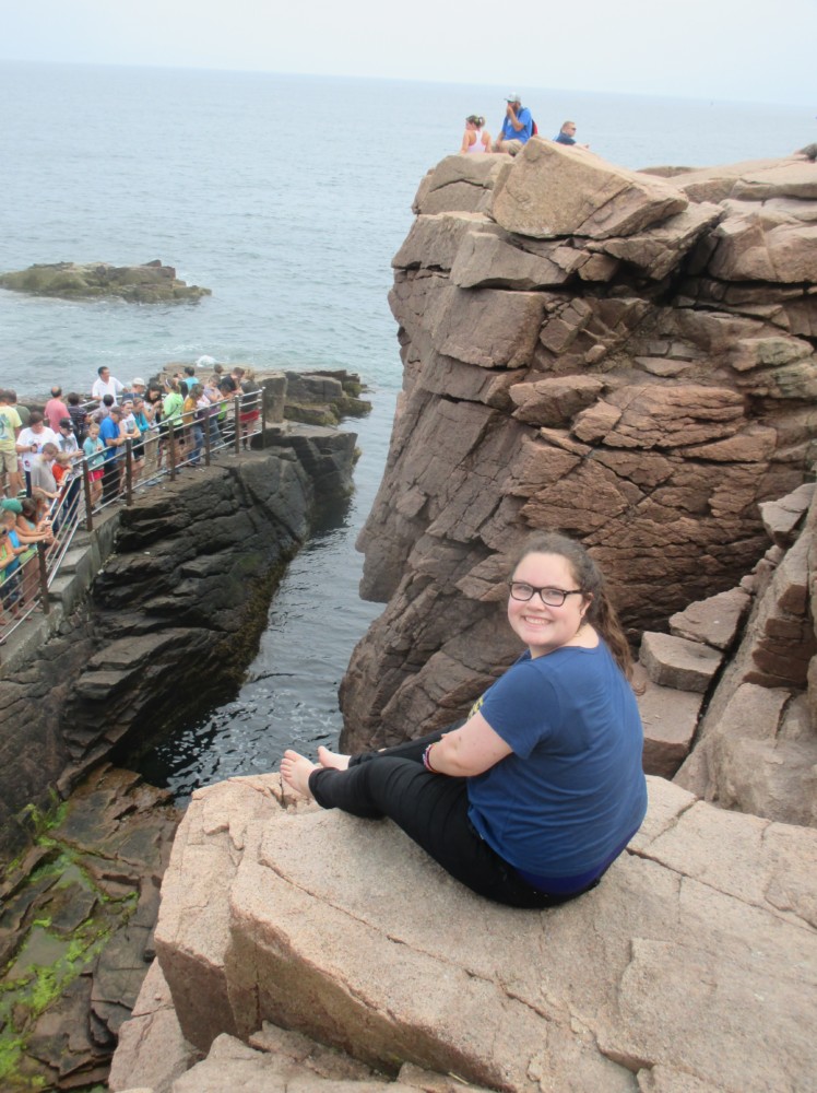 A teen sits upon a rock near the ocean during a retreat for Beyond Akeela's neurodivergent college readiness program. 
