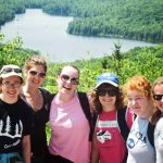 Campers and staff posing at a lookout above a lake after a day hike, one of the trips the hiking and camping director leads